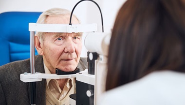 An elder man receives a slit lamp eye exam