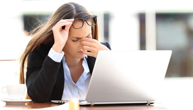 A woman in front of a laptop rubbing her eyes