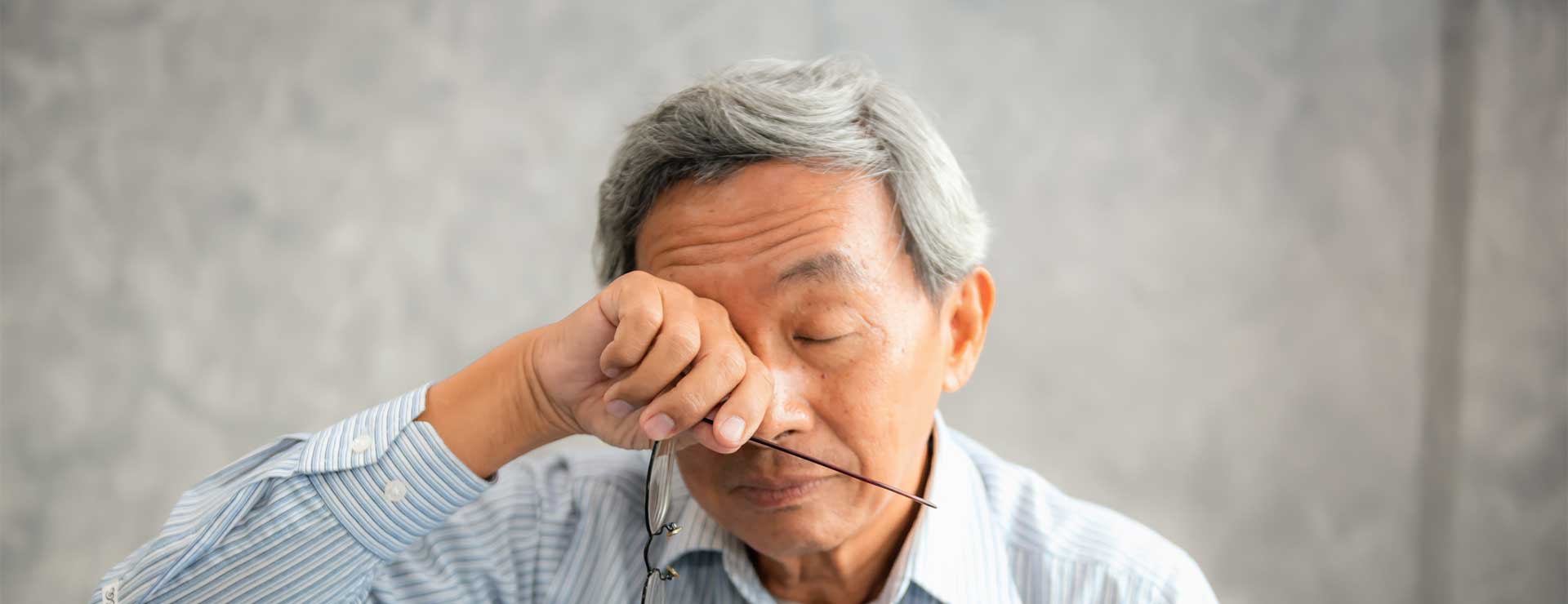 senior man rubs eyes holding glasses