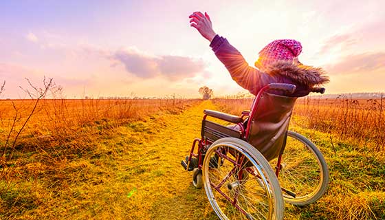 girl in wheelchair outside with arms up in joy