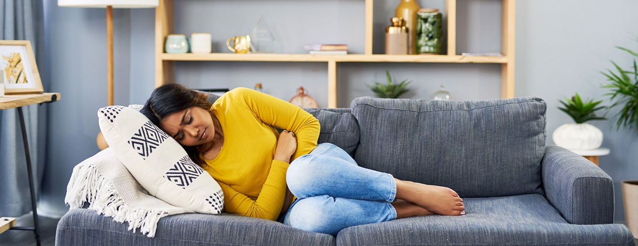 A woman on the couch holding her stomach from ovarian cyst pain