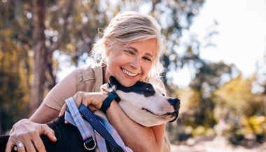Older woman hugging her dog outdoors in nature