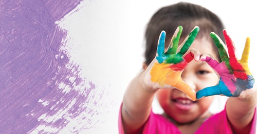 A child makes a heart with their painted hands