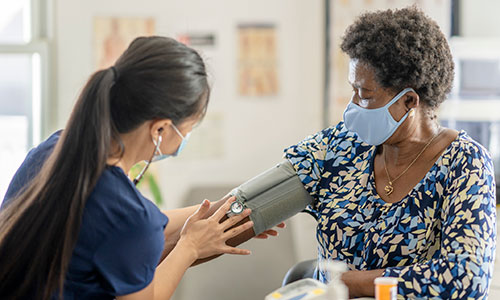 A masked nurse checks a masked patient's blood pressure