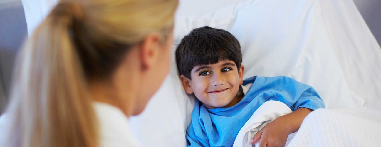 A child smiles at his doctor from his hospital bed.