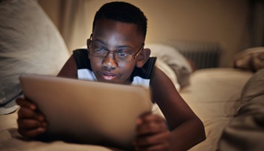 Young boy using tablet in bed