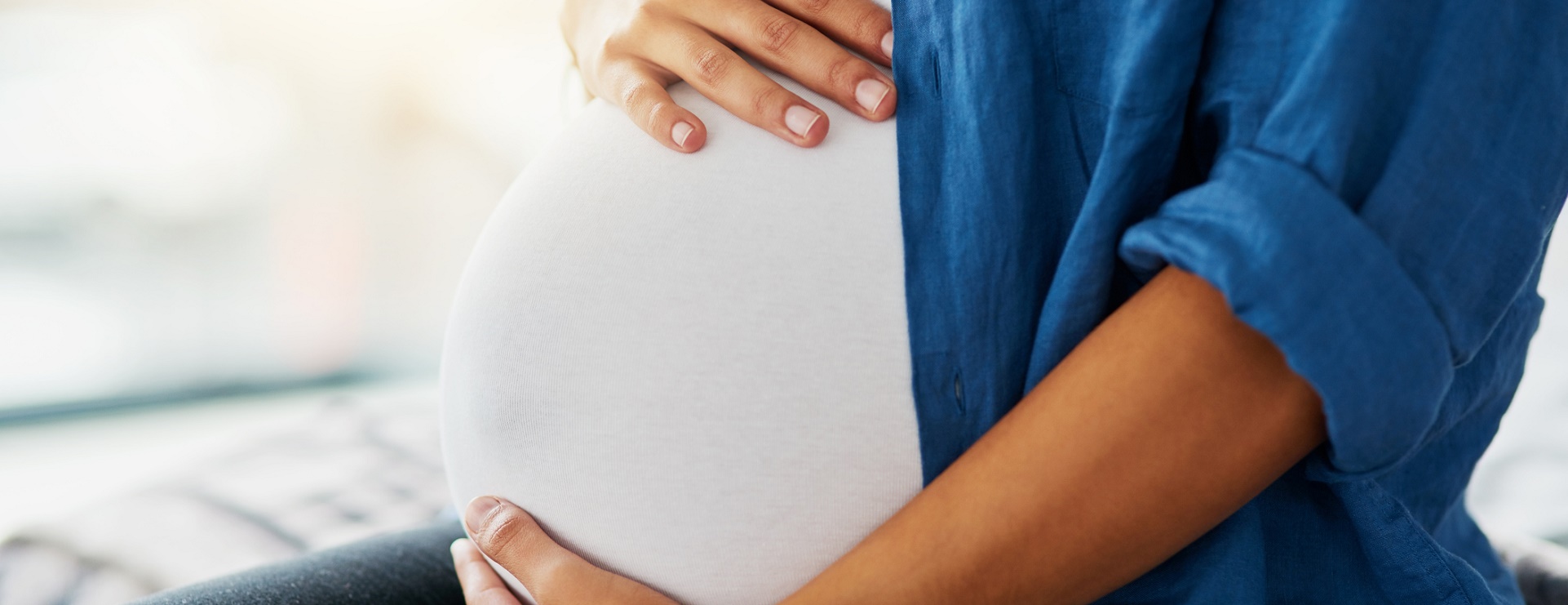 Close up on a pregnant woman wearing a jean jacket, holding her belly