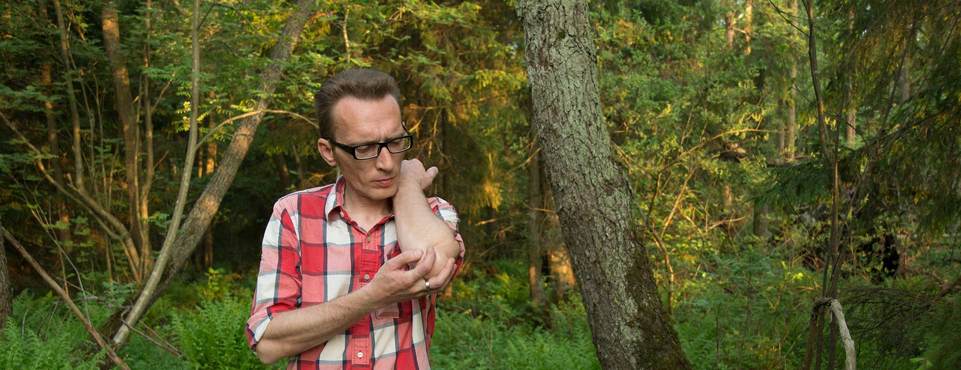 A man scratches at a mosquito bite in the woods.