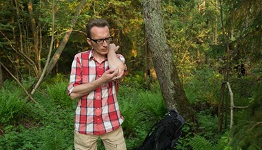 A man scratches at a mosquito bite in the woods.