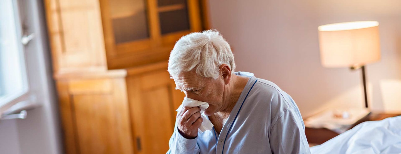 Elderly man blows his nose into tissue
