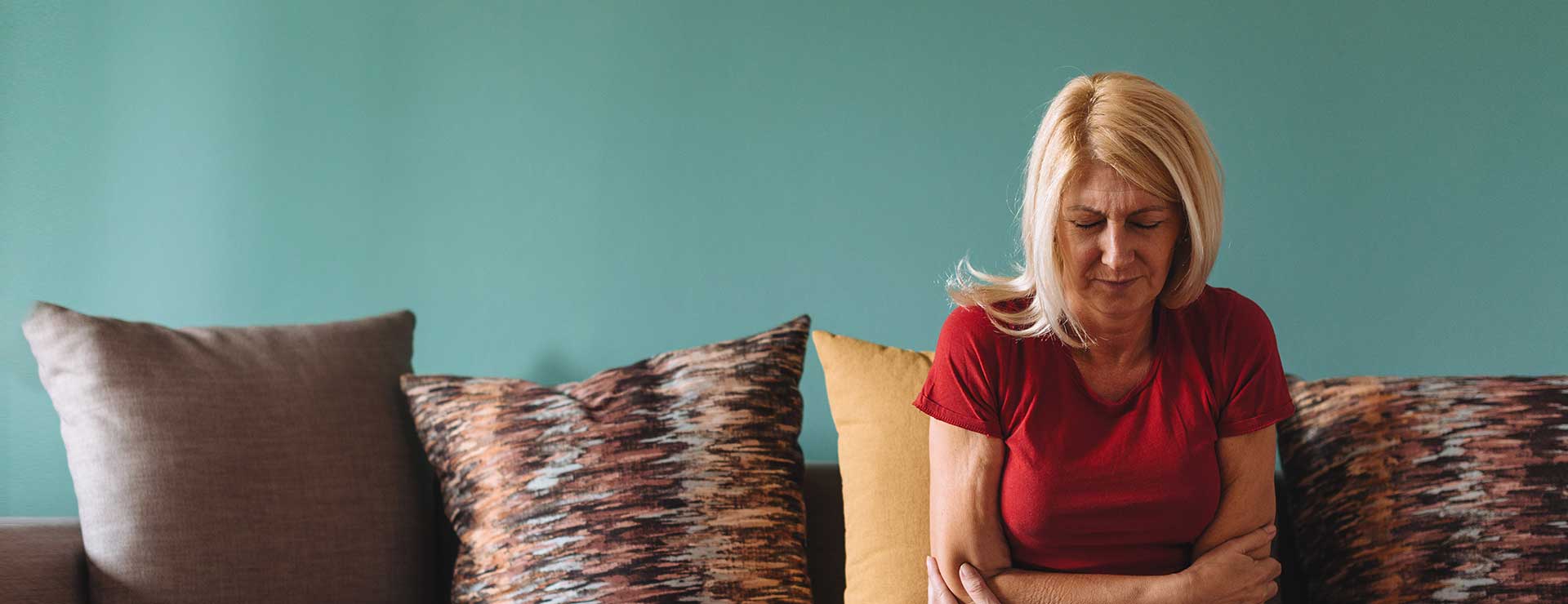 An older woman sits on the couch, hunched over in pain.
