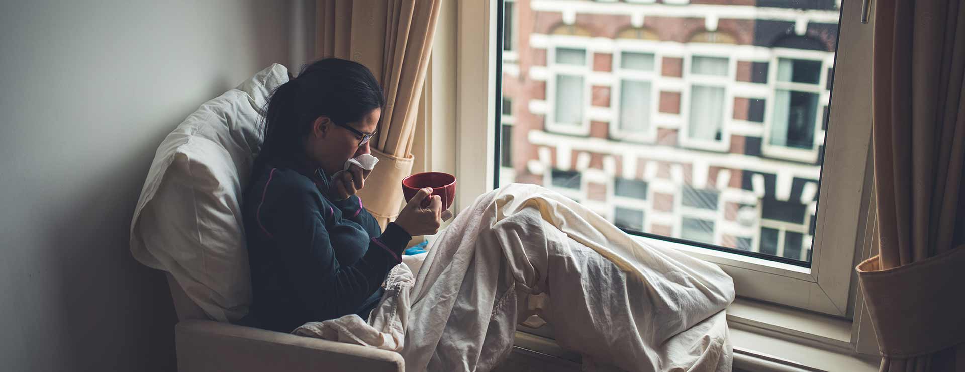 A woman sits by the window, sick with an upper respiratory infection.