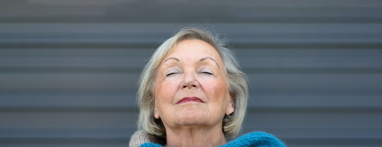 A senior woman takes a deep breath outside.