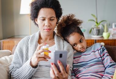 Mom holding a medicine bottle while her unwell child leans on her shoulder
