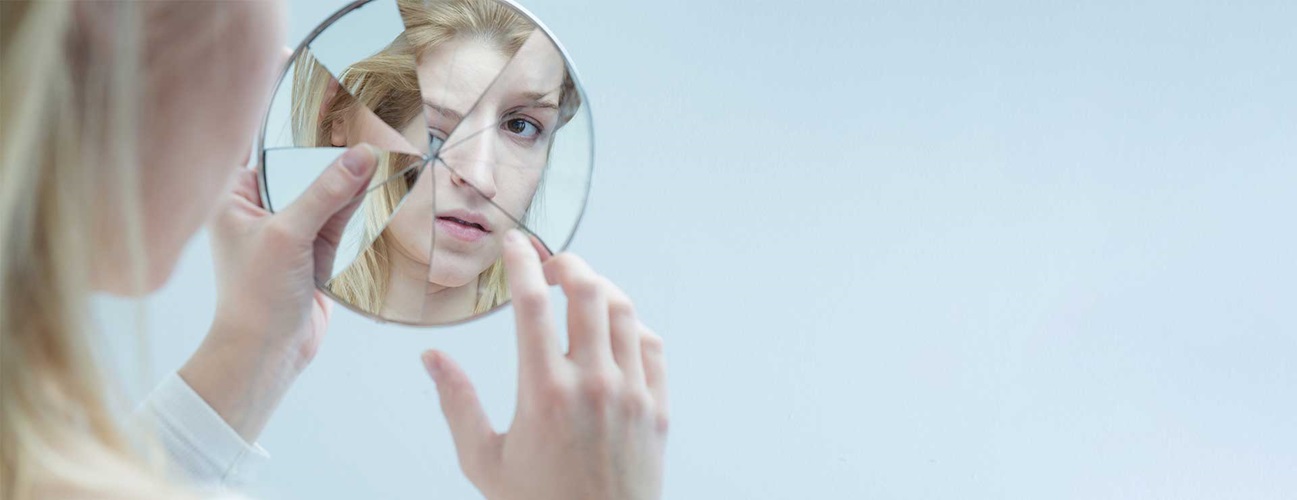Woman looking at her face in a broken mirror.