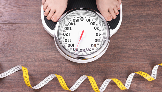 Person stepping on scale with tape measure