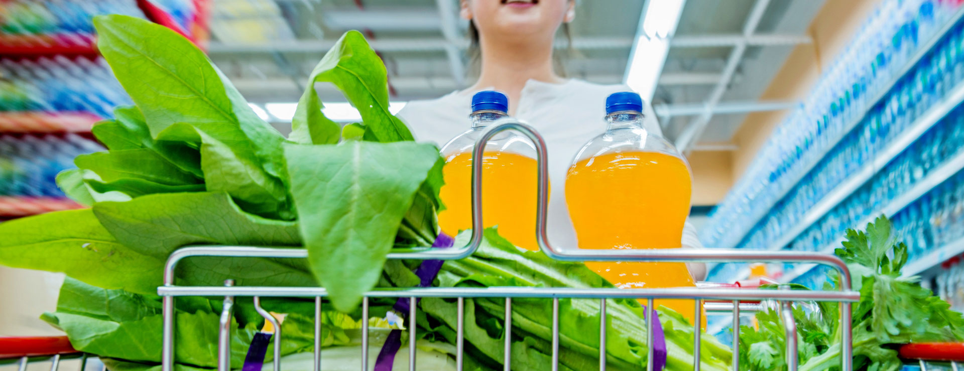 A young person grocery shopping with greens and juice in the cart