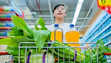 A young person grocery shopping with greens and juice in the cart