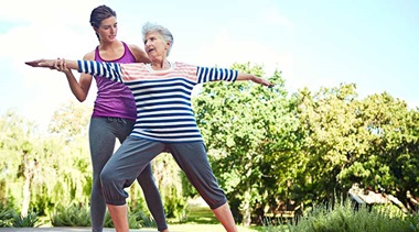 A yoga instructor assists a senior with her posture.