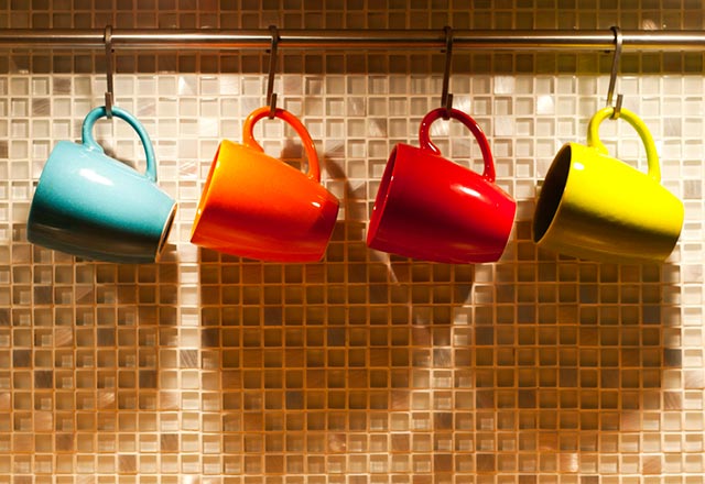 A collection of colorful coffee mugs hang beneath a cabinet.