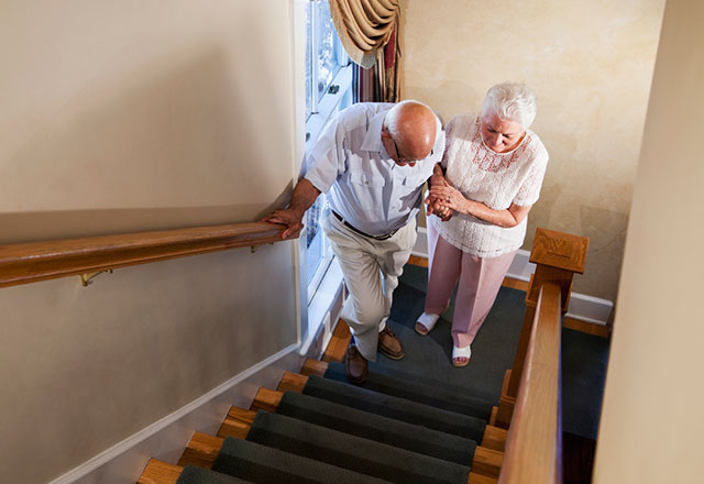 A senior woman helps her husband go up the stairs.