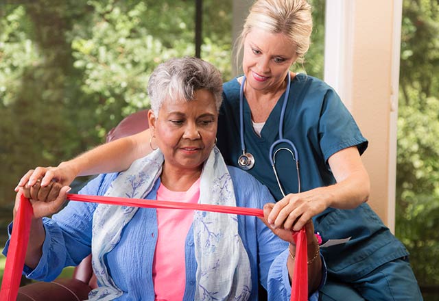 A physical therapist assists a senior woman as she exercises using a resistance band.