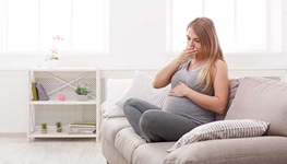 A pregnant woman suffers heartburn while sitting on the couch.