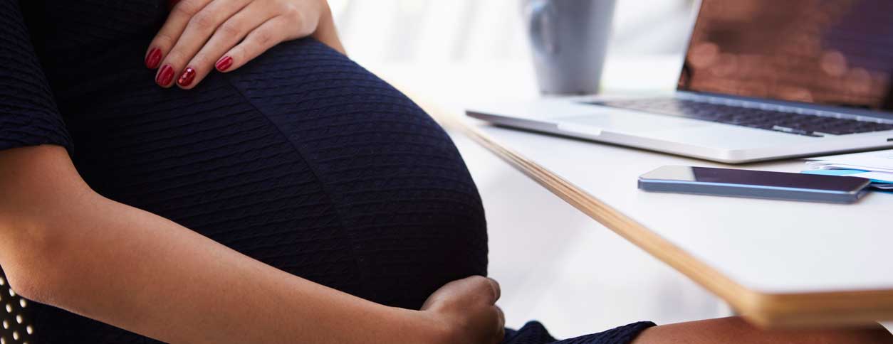 Pregnant woman holding belly at desk