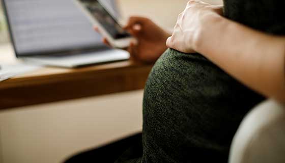 Pregnant woman sits at her desk with a mobile phone.