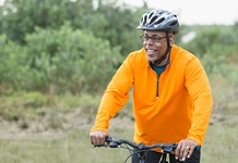 Older gentleman riding a bike through a wooded trail. 