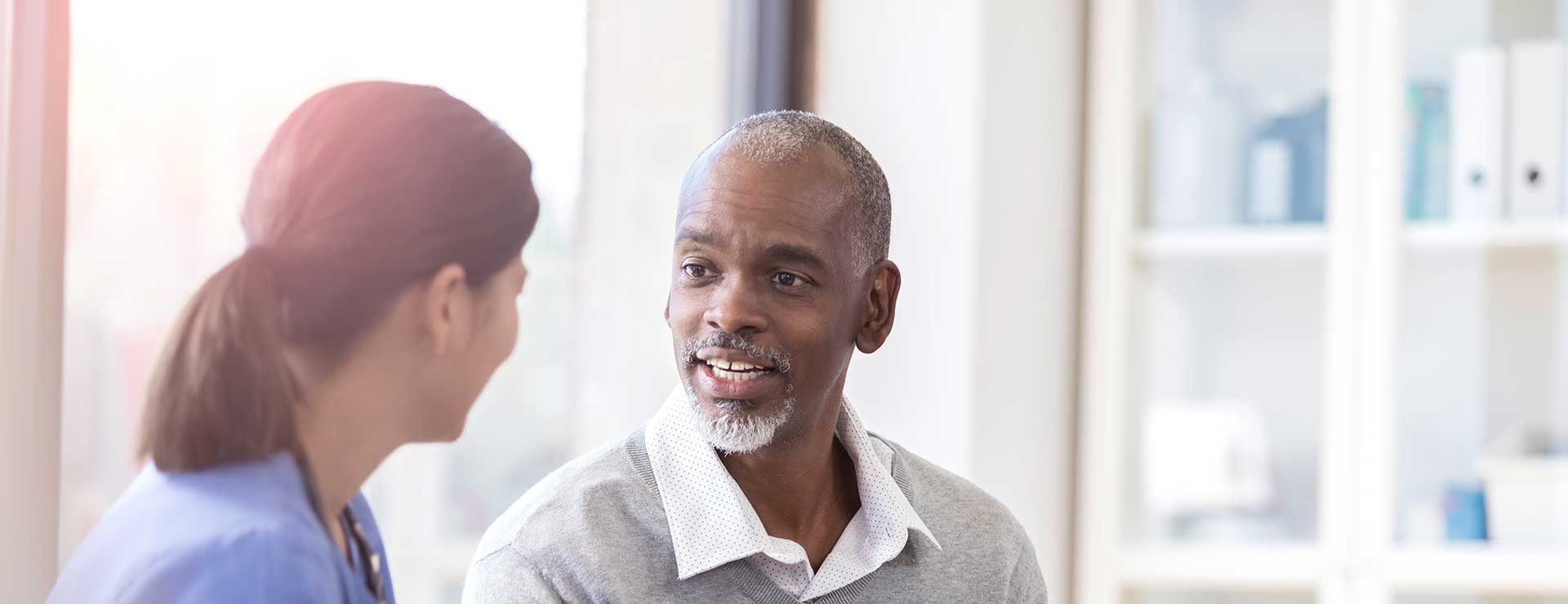An older man consults with nurse during exam