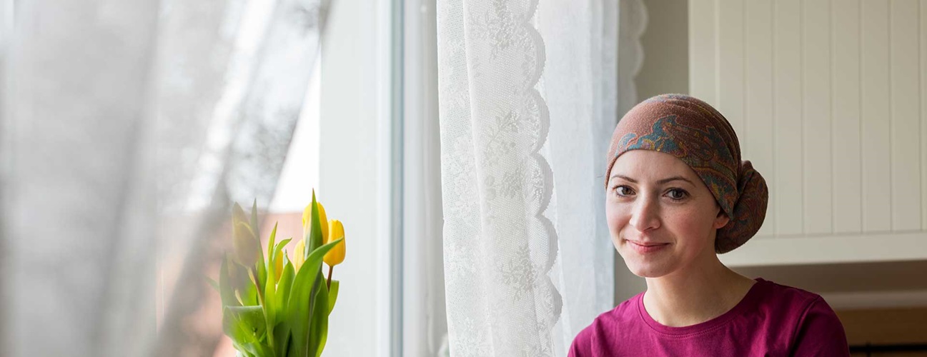 A young cancer patient sits in front of a window.