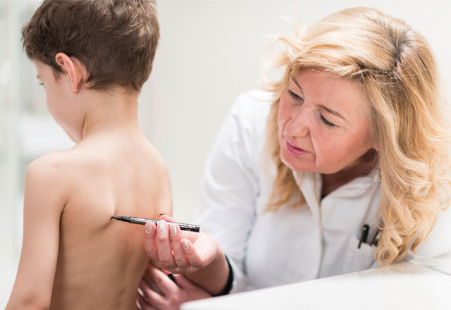 a pediatrician screens a boy for scoliosis