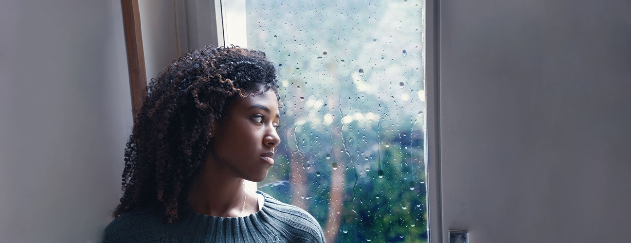 person stares out a window with raindrops on it
