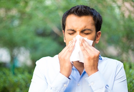 Man sneezing outdoors and covering his nose