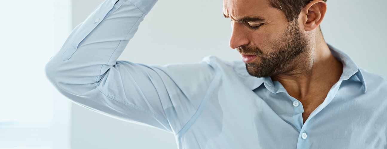 hyperhidrosis excessive sweating - man looking at sweat from underarm on light blue shirt