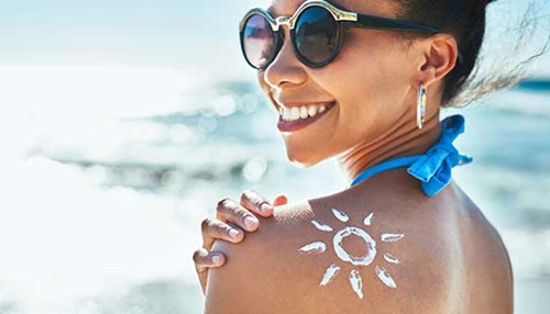 mulher sorri com sol desenhado em loção no ombro
