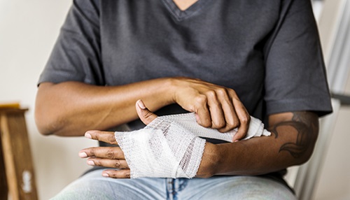 A person carefully wraps their arm in gauze.