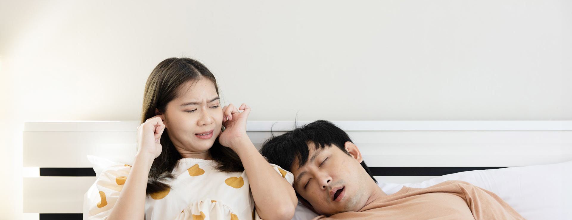 Woman covering her ears as her husband snores on her shoulder