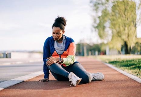 Female athlete sitting on a running track with an injured knee.