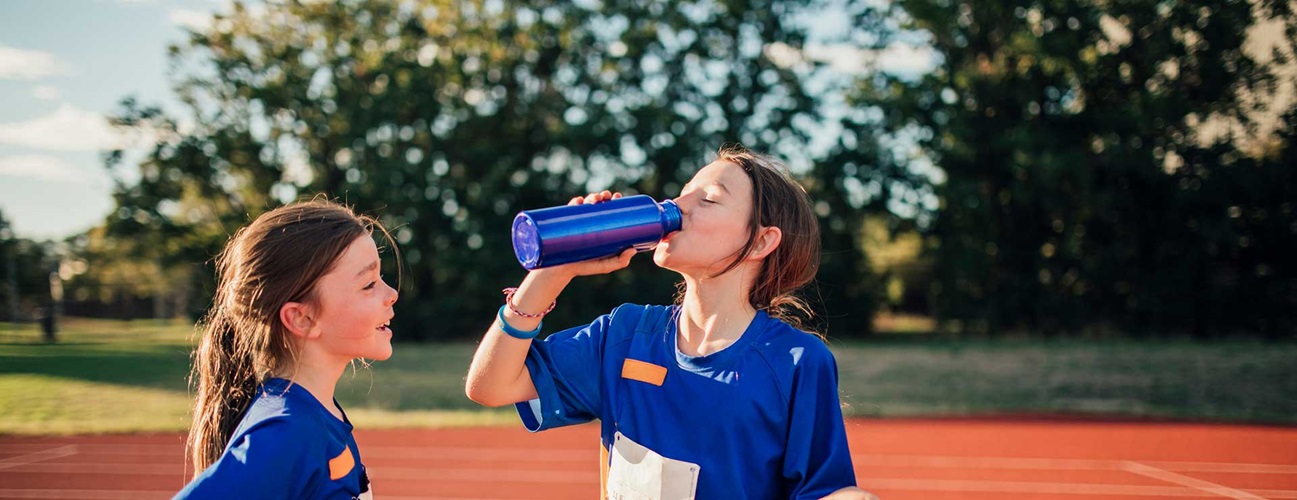 Two girls on a track field drinking water after training