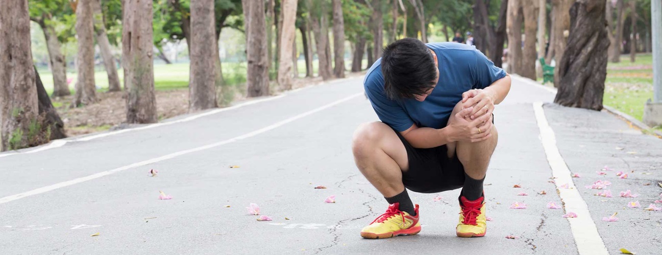 Runner crouched holding knee on running path 