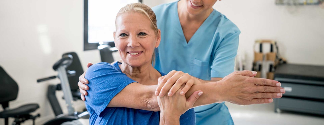 Physical therapist holding senior patient while she stretches her shoulder