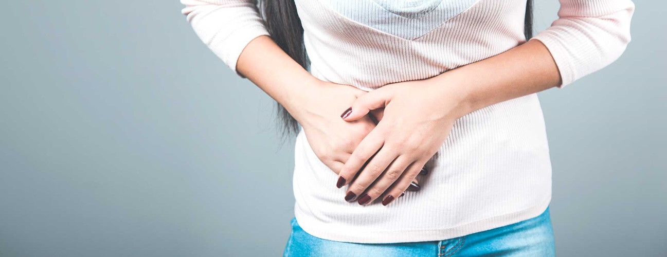 Woman in light sweater and jeans clutching the right side of her stomach in pain