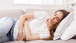 woman clutching stomach on sofa