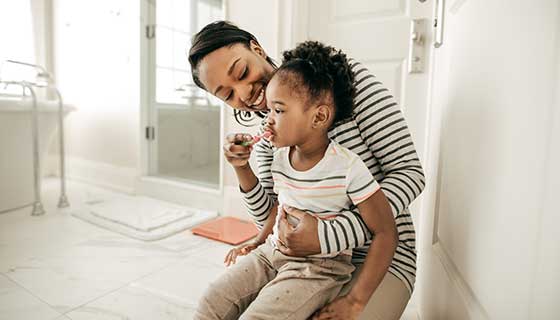 young mother helping child brush teeth