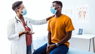 Masked doctor talking with patient in office