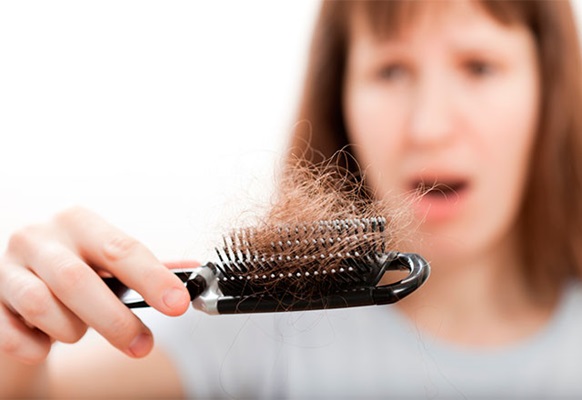 Woman looks frustratingly at hair loss on brush