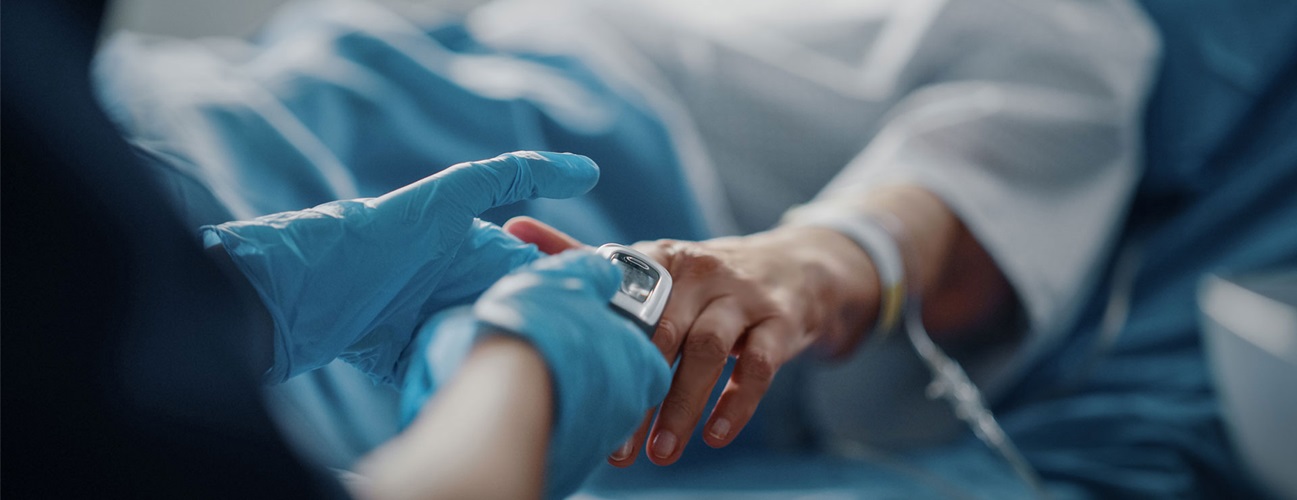 gloved hands hold hand of patient with IV