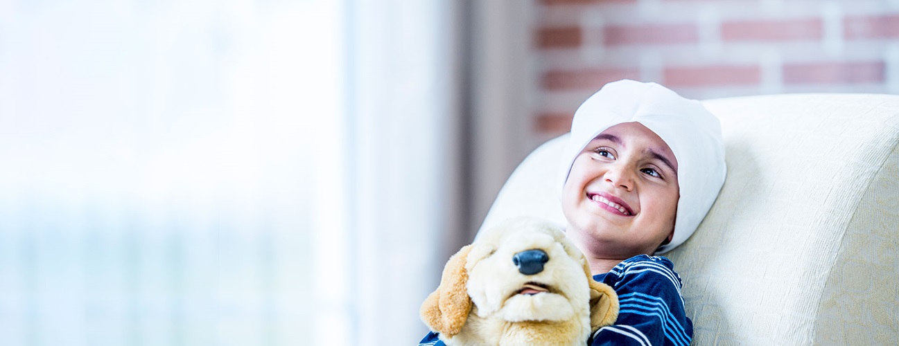 A young cancer patient holds a stuffed dog plush